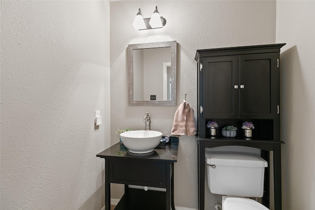 half bath featuring toilet, a textured wall, and vanity