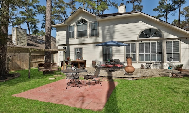 rear view of property with a deck, a lawn, fence, and a chimney