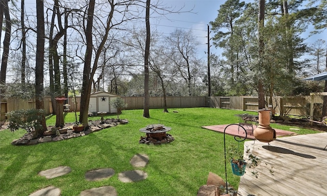 view of yard featuring an outbuilding, a deck, a fenced backyard, a fire pit, and a shed