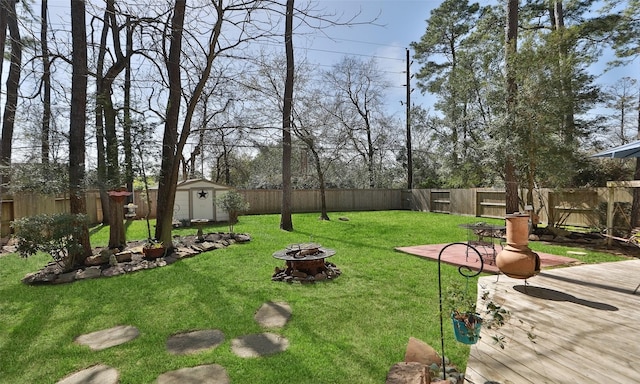 view of yard featuring a storage shed, an outdoor fire pit, a wooden deck, and a fenced backyard
