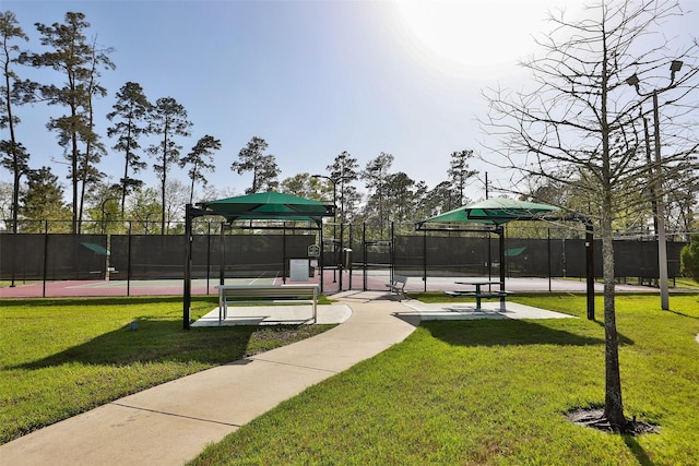 view of home's community with a tennis court, a lawn, and fence