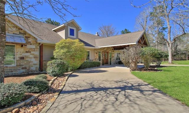 view of front of home featuring a front yard, stone siding, roof with shingles, and driveway