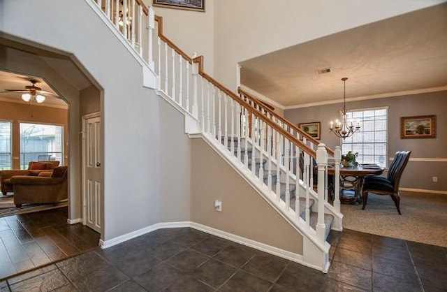 staircase with visible vents, ornamental molding, ceiling fan with notable chandelier, a high ceiling, and baseboards