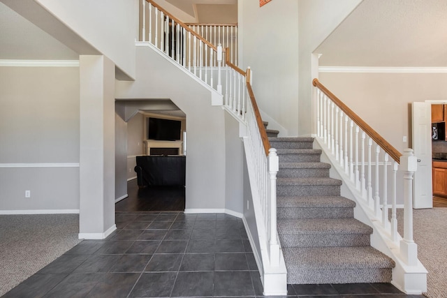 staircase featuring tile patterned flooring, crown molding, a high ceiling, and baseboards