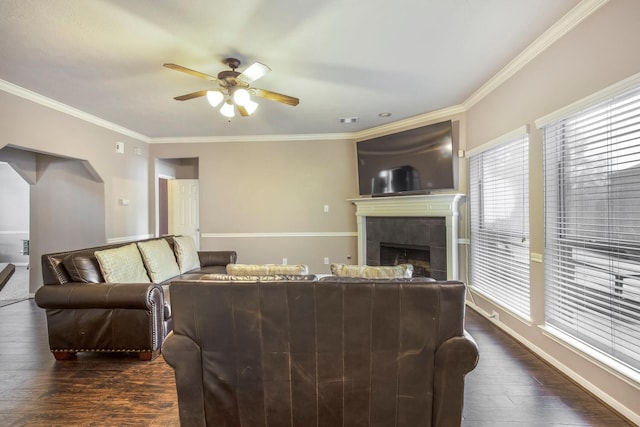 living area with visible vents, a tile fireplace, ceiling fan, dark wood-type flooring, and crown molding