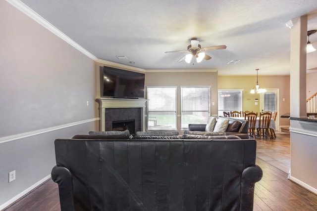 living area featuring dark wood-type flooring, baseboards, ornamental molding, ceiling fan with notable chandelier, and a tile fireplace