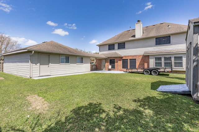 back of house featuring a lawn, roof with shingles, brick siding, a chimney, and a patio area