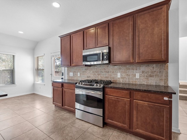 kitchen with light tile patterned floors, lofted ceiling, stainless steel appliances, backsplash, and dark stone counters