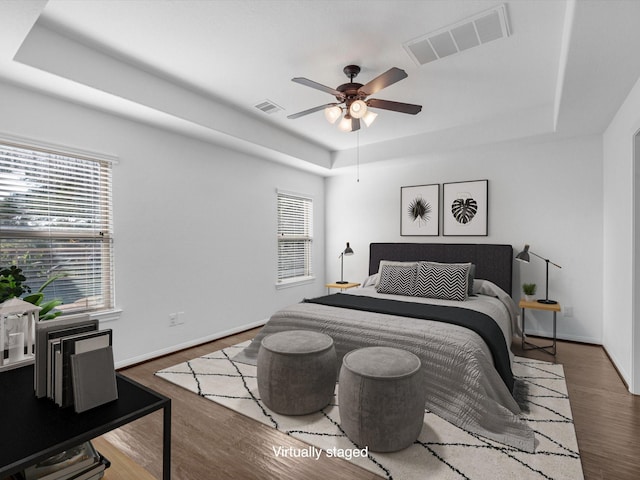 bedroom featuring a raised ceiling, visible vents, baseboards, and wood finished floors