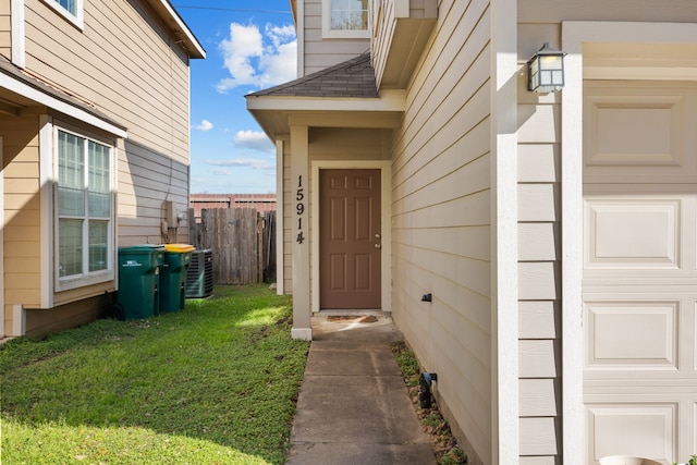 entrance to property with a garage, central AC, fence, roof with shingles, and a lawn