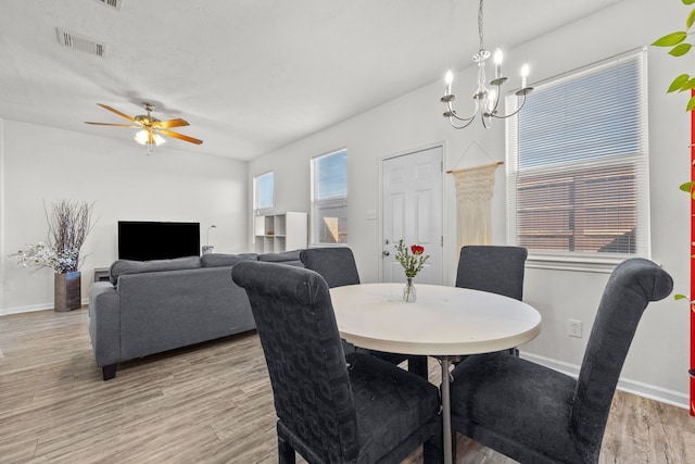 dining space with ceiling fan with notable chandelier, light wood-style flooring, visible vents, and baseboards