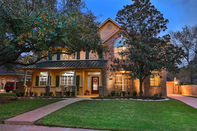 view of front of property with a standing seam roof, covered porch, fence, a front yard, and brick siding