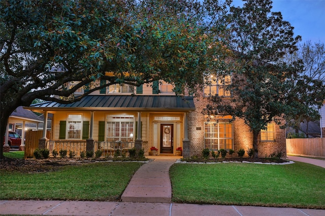 view of front of home with metal roof, brick siding, fence, a standing seam roof, and a front yard