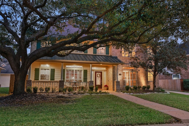 view of front of home with metal roof, covered porch, brick siding, a front lawn, and a standing seam roof