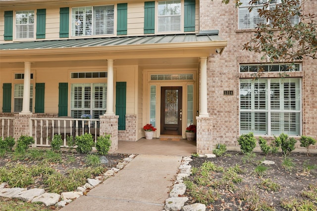 view of exterior entry with covered porch, a standing seam roof, metal roof, and brick siding