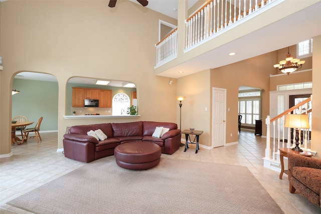 living room featuring arched walkways, ceiling fan with notable chandelier, light tile patterned flooring, and baseboards