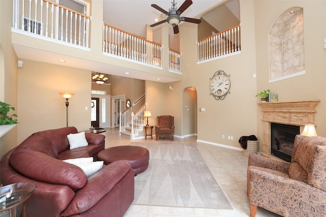 living area featuring baseboards, arched walkways, a glass covered fireplace, ceiling fan, and stairs