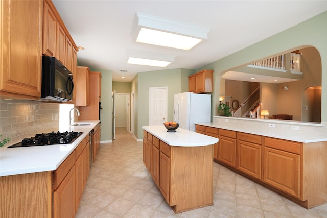 kitchen featuring a sink, light countertops, backsplash, a center island, and black appliances