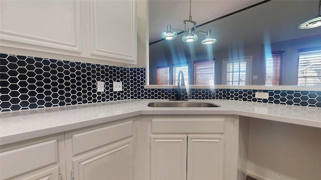 kitchen with a sink, decorative light fixtures, white cabinets, light countertops, and decorative backsplash