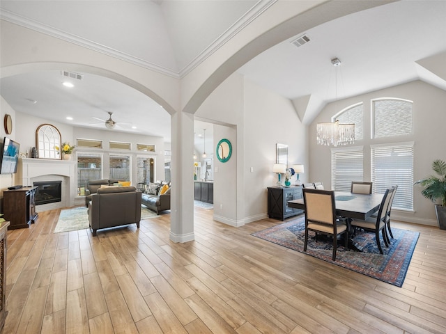 dining room with light wood-type flooring, high vaulted ceiling, visible vents, and a glass covered fireplace