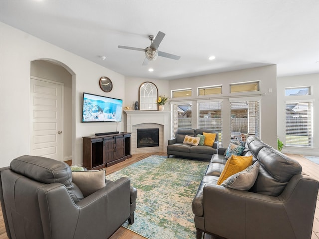 living area featuring arched walkways, wood finished floors, a glass covered fireplace, and recessed lighting