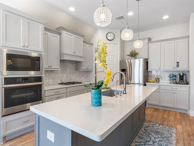 kitchen with light countertops, appliances with stainless steel finishes, a center island with sink, and visible vents