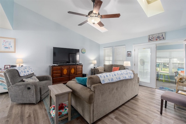 living area featuring vaulted ceiling with skylight, a ceiling fan, and light wood finished floors