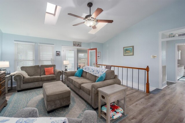 living room featuring lofted ceiling with skylight, wood finished floors, baseboards, and ceiling fan