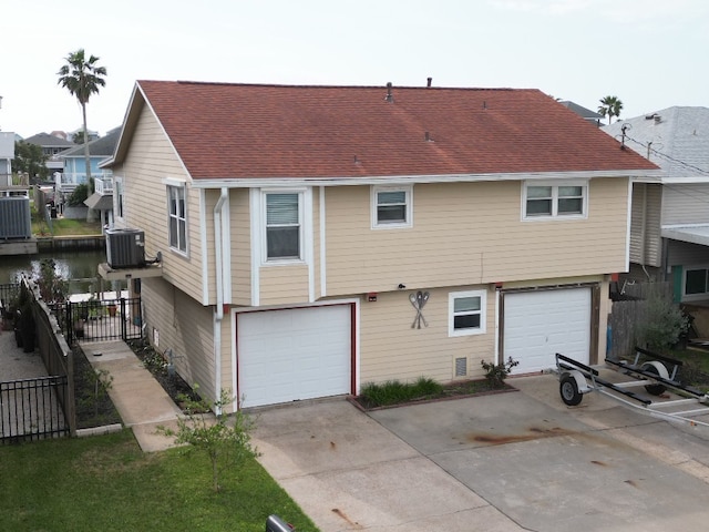 back of property featuring fence, driveway, central AC, a shingled roof, and a garage