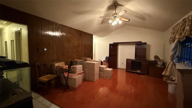 living area with wooden walls, a ceiling fan, wood finished floors, lofted ceiling, and a textured ceiling