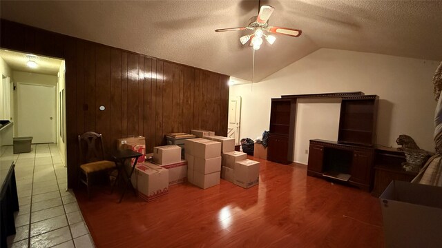 interior space featuring wooden walls, a ceiling fan, wood finished floors, lofted ceiling, and a textured ceiling