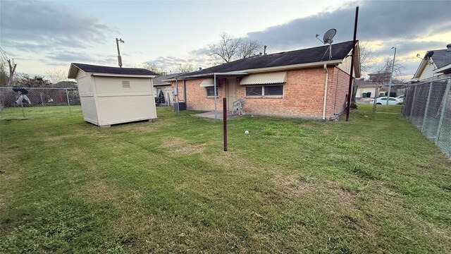 back of property featuring brick siding, a lawn, an outdoor structure, and a fenced backyard