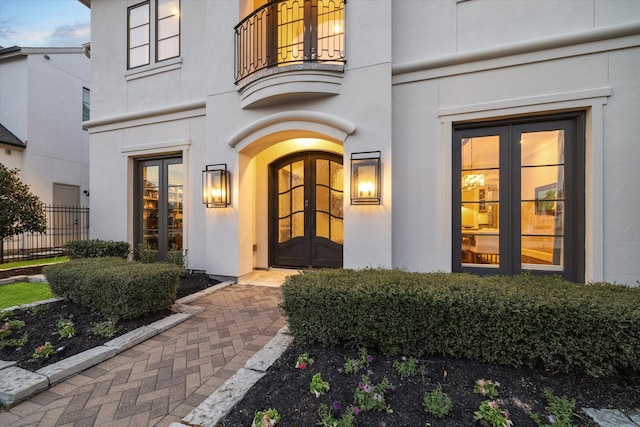 entrance to property featuring a balcony, french doors, fence, and stucco siding