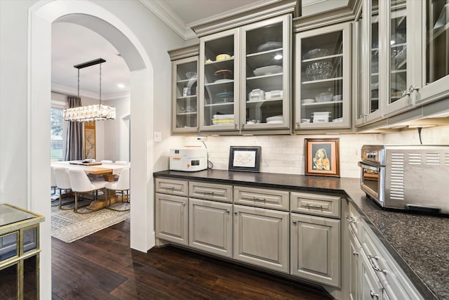 kitchen with tasteful backsplash, dark wood-style floors, arched walkways, crown molding, and glass insert cabinets