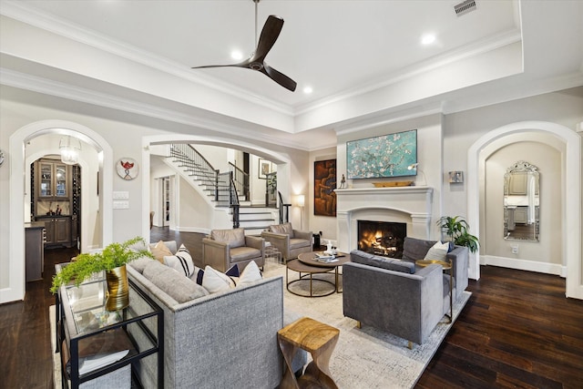 living room featuring visible vents, a tray ceiling, arched walkways, wood-type flooring, and ceiling fan