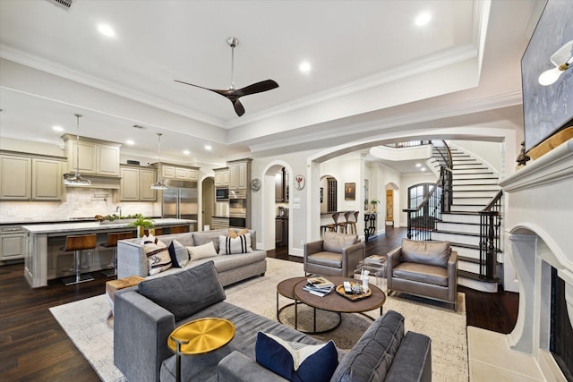 living area with arched walkways, a raised ceiling, crown molding, and ceiling fan