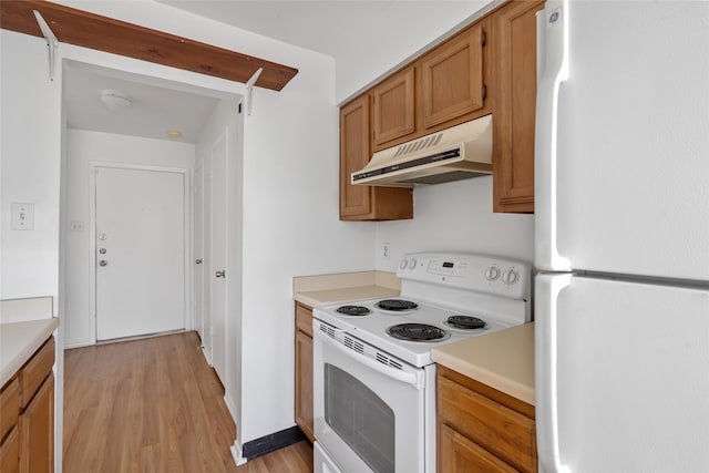 kitchen with brown cabinets, light countertops, light wood-type flooring, white appliances, and under cabinet range hood