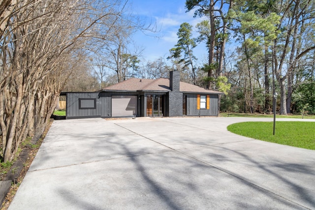 view of front facade featuring concrete driveway, a front lawn, board and batten siding, and a chimney