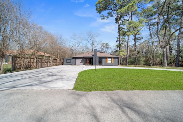 view of front of house with concrete driveway, fence, a chimney, and a front lawn