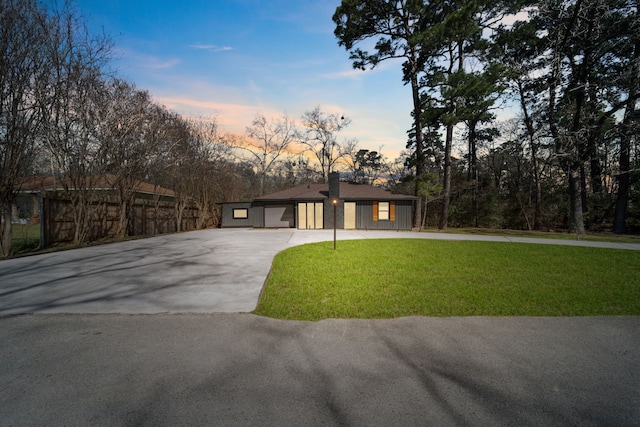 view of front of property featuring driveway, a lawn, and fence