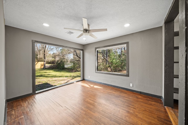 unfurnished room with baseboards, a textured wall, a textured ceiling, and hardwood / wood-style floors