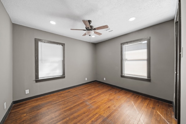 empty room with visible vents, a textured ceiling, baseboards, and hardwood / wood-style flooring