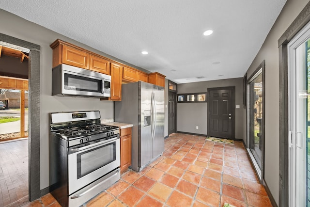 kitchen with appliances with stainless steel finishes, light countertops, a textured ceiling, and baseboards