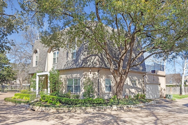 view of front of home featuring mansard roof, fence, and driveway