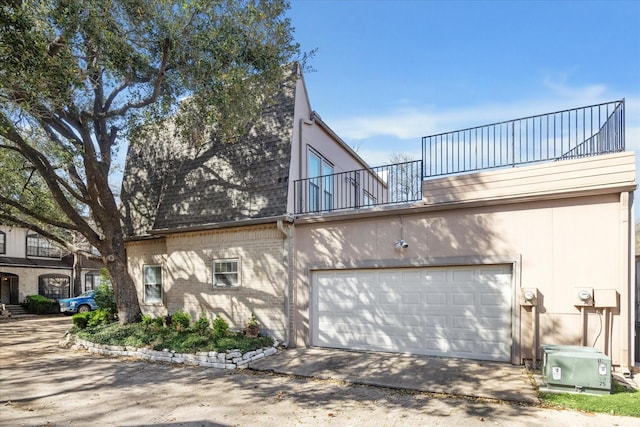 view of property exterior featuring a garage, brick siding, roof with shingles, and a balcony