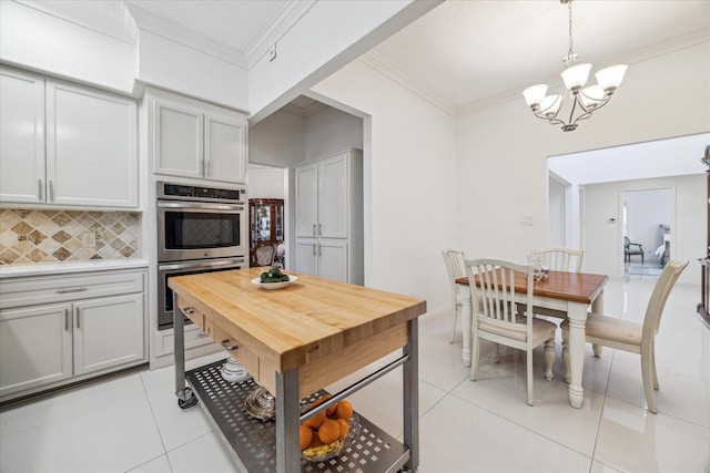 kitchen with tasteful backsplash, stainless steel double oven, crown molding, and light tile patterned floors