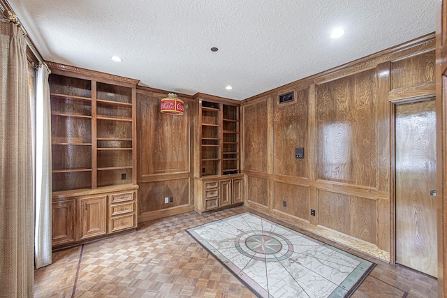 interior space with a textured ceiling, recessed lighting, and wooden walls