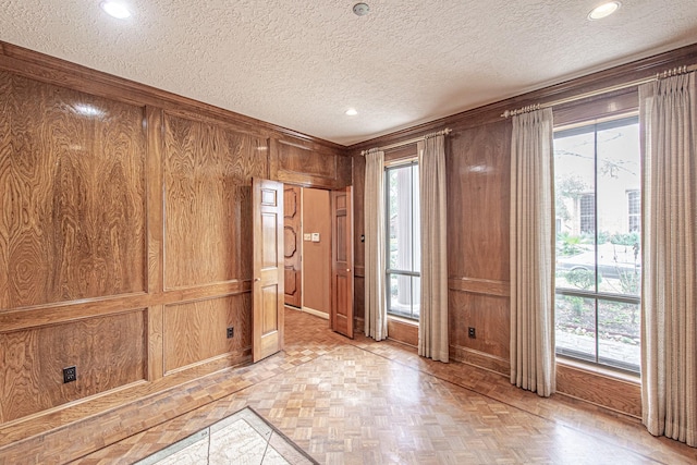 spare room with a textured ceiling, recessed lighting, and wooden walls