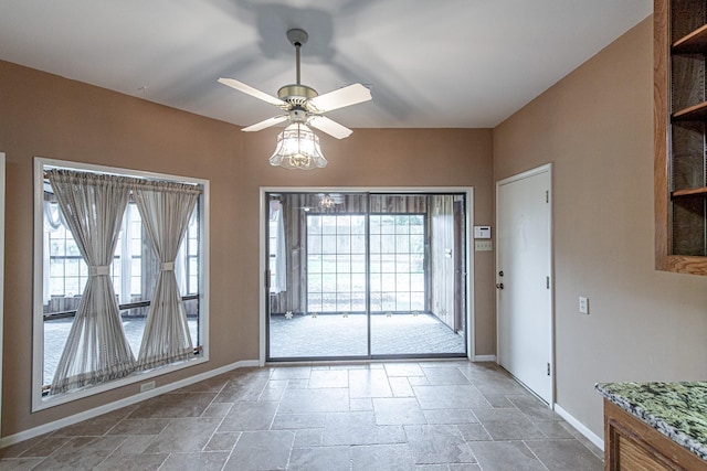 doorway to outside featuring a ceiling fan, stone tile flooring, and baseboards