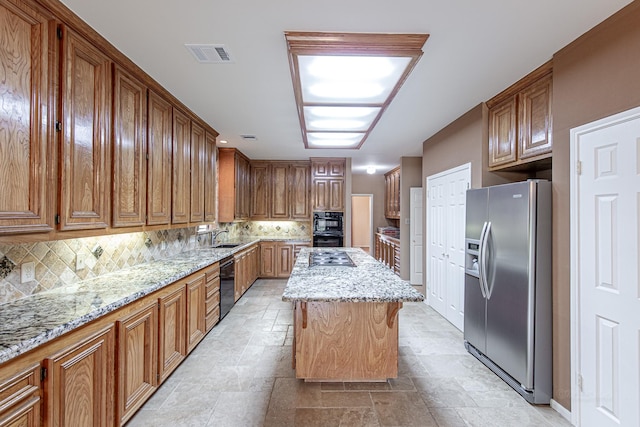 kitchen with a kitchen island, visible vents, black appliances, tasteful backsplash, and stone finish floor